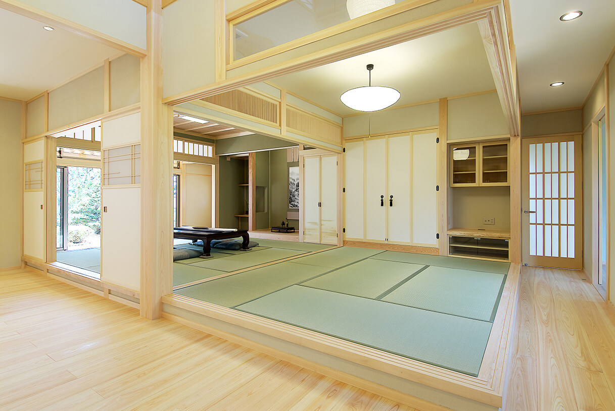 明るい木製フローリングの通路から、和室と、その奥に別の和室が連なる伝統的な日本の家屋の内部