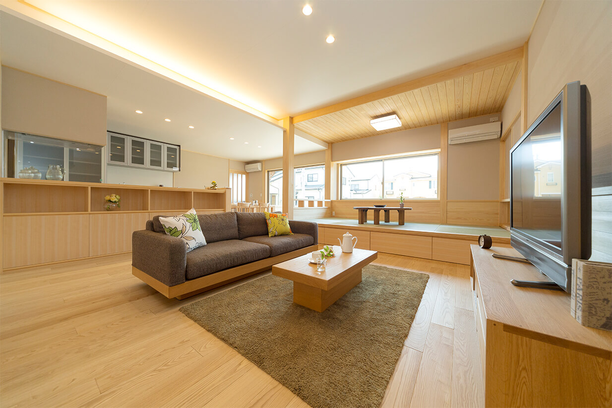 明るいリビングルームで、中央にソファと木製のローテーブル、右奥に和風の小上がりが配置されている