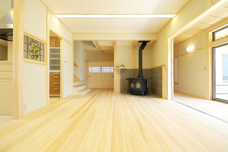 明るい木製フローリングの広々としたLDK空間に、黒い薪ストーブが設置されている、福井県の住宅