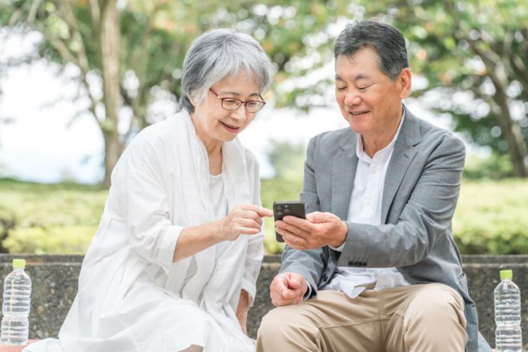 ベンチに座ってスマホを見る老夫婦